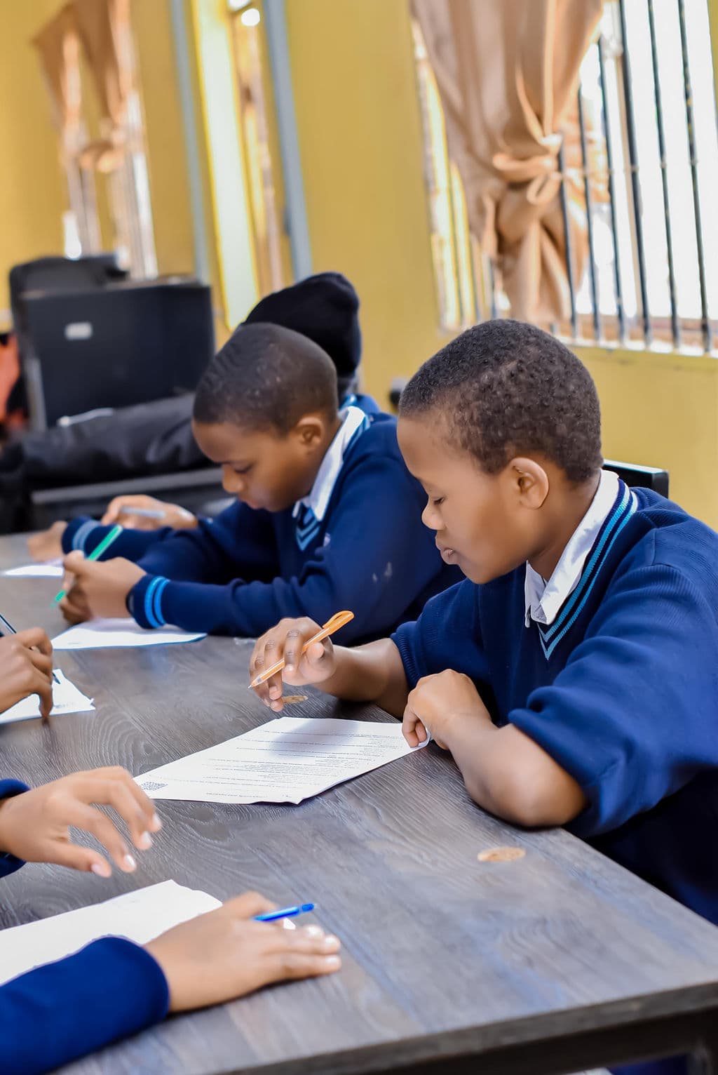 Students writing on paper at a classroom table